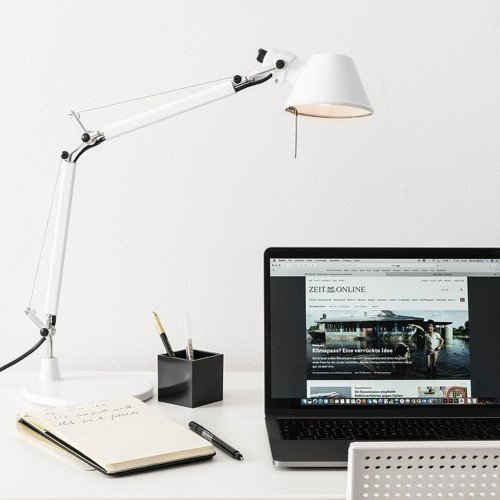 Tolomeo Mini blanca sobre escritorio doméstico junto a portátil. Tolomeo Mini blanca sobre escritorio doméstico junto a portátil.