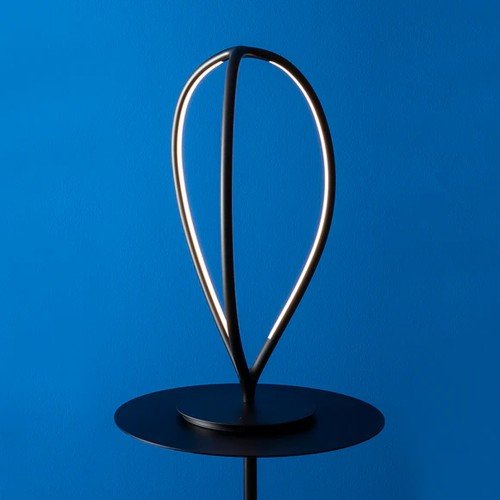 Arrival table encendida en acabado negro mate sobre mesa auxiliar con pared azul Arrival table encendida en acabado negro mate sobre mesa auxiliar con pared azul