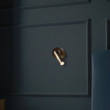 Aplique LEDtube A Marset bronce sobre pared azul oscura con iluminación cálida